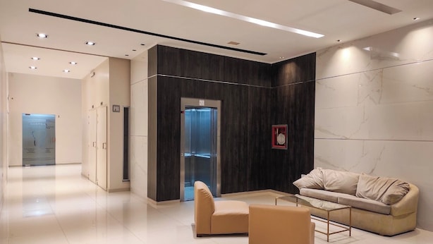Eine moderne Lobby mit Empfangstresen, einer Wartezone inklusive Sofa und Sesseln sowie einem Glaselevator.