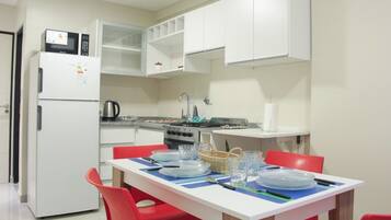 Una cocina compacta con armarios blancos, un refrigerador, una estufa y una mesa de comedor con sillas rojas.