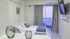 Ein Hotelzimmer mit Bett, Wandfernseher und Balkon mit Vorhängen.