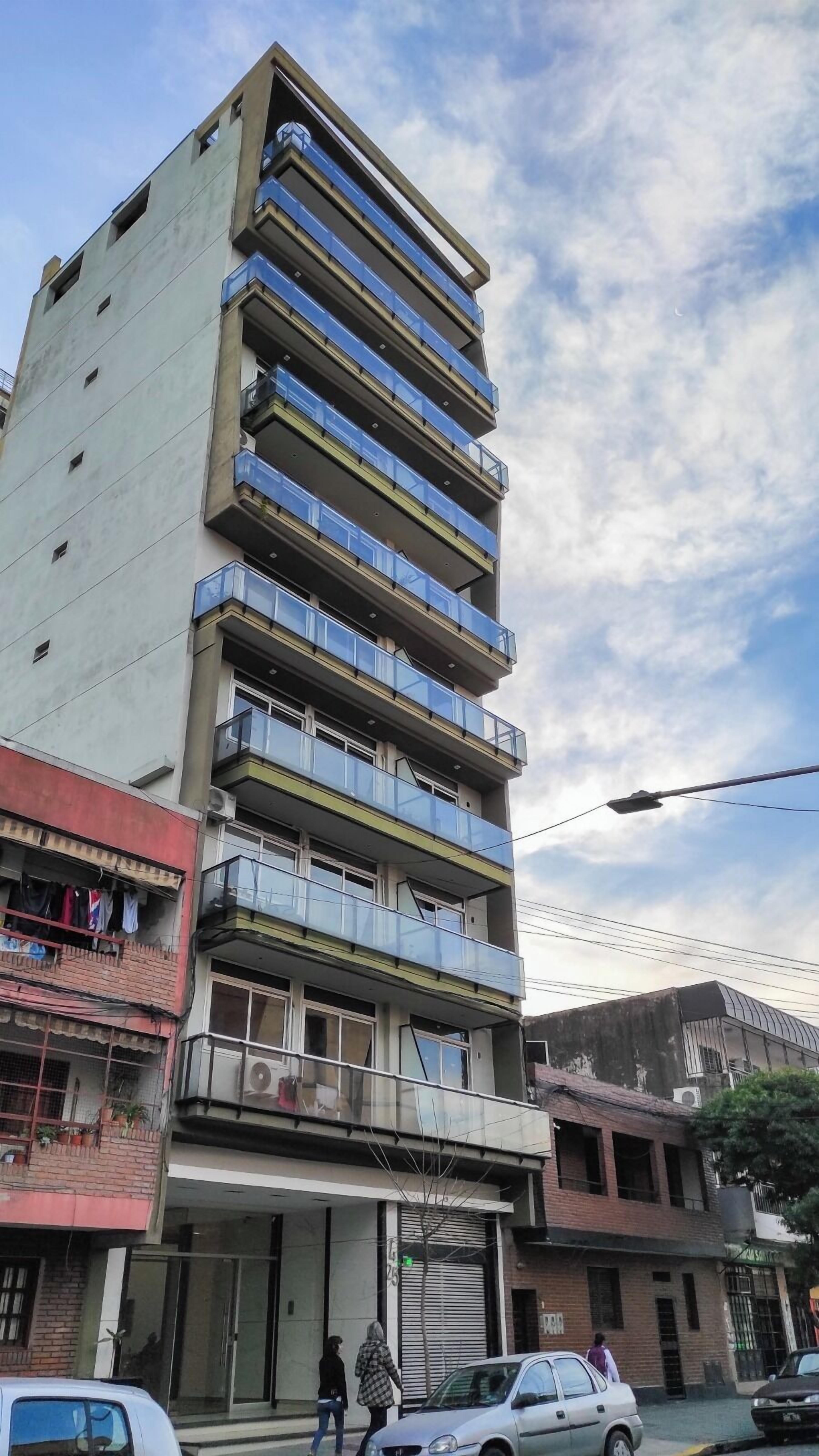 A multi-story building with balconies, a storefront, and a parked car.