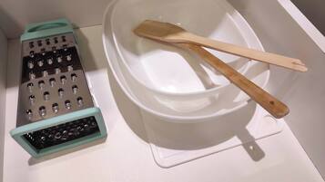 A kitchen with a white countertop, a green and silver grater, and a white bowl with a wooden spatula.