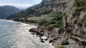 Paesaggio costiero con scogliere rocciose, una spiaggia e vista sul mare.