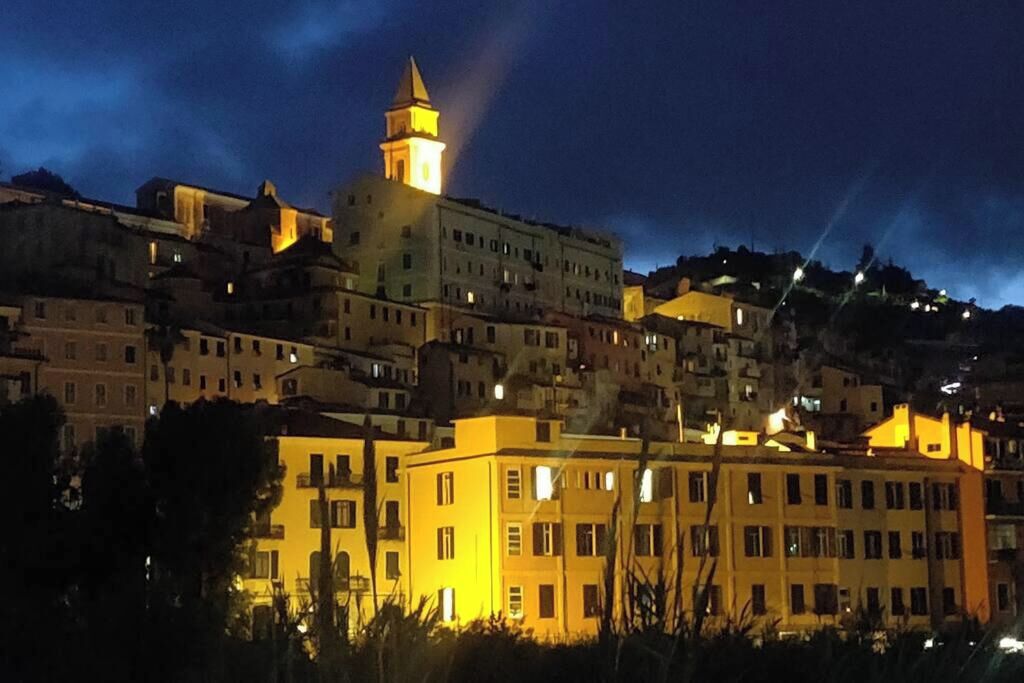 Una vista nocturna de un pueblo en una ladera con edificios iluminados y una torre destacada.