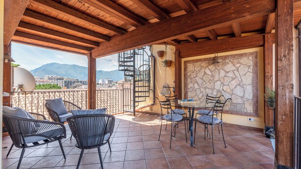 A covered outdoor patio with wooden beams, a stone wall, and a view of mountains. - Le terrazze nel cuore della Kalsa by Wonderful Italy (Palermo)