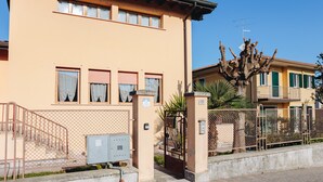 Un edificio de dos pisos con fachada color beige, una reja metálica y una escalera que lleva a la entrada.