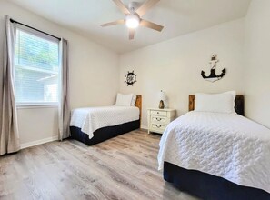 A bedroom with two beds, a ceiling fan, a window with curtains, a nightstand, and a wall clock. - Seas the Day ¤ 3 mins to Florida #1 beach! (St. Augustine)