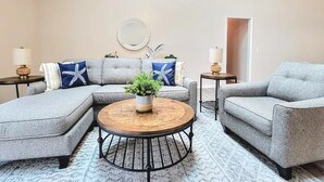 A modern living room with a grey sectional sofa, a round coffee table with a plant, and two armchairs. - Seas the Day ¤ 3 mins to Florida #1 beach! (St. Augustine)