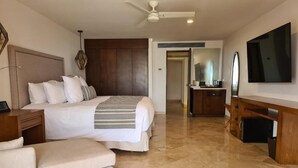 A hotel room with a large bed, a desk with a mirror, a television, and a ceiling fan.