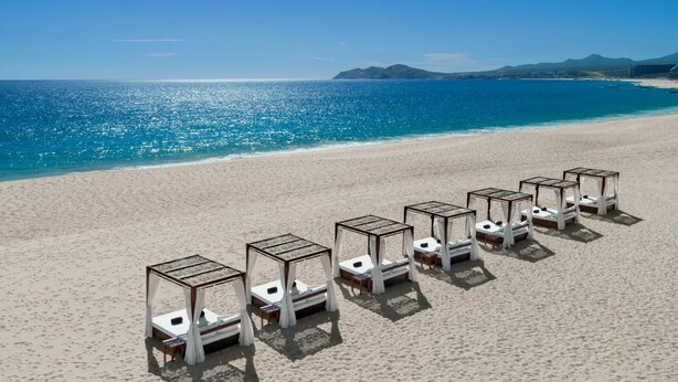 A beach with rows of sunbeds and a clear view of the ocean and distant mountains.