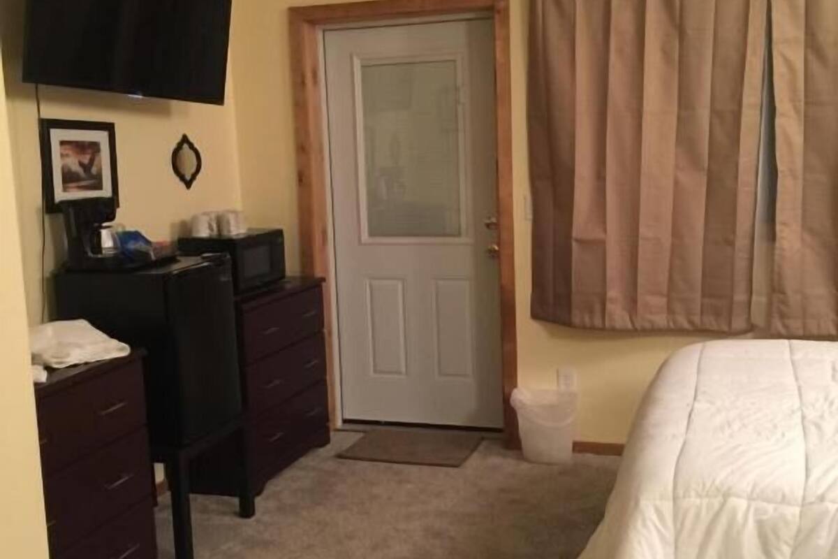 A bedroom with a bed, a desk, a chair, a television, and a door.