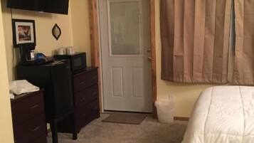 A bedroom with a bed, a desk, a chair, a television, and a door.