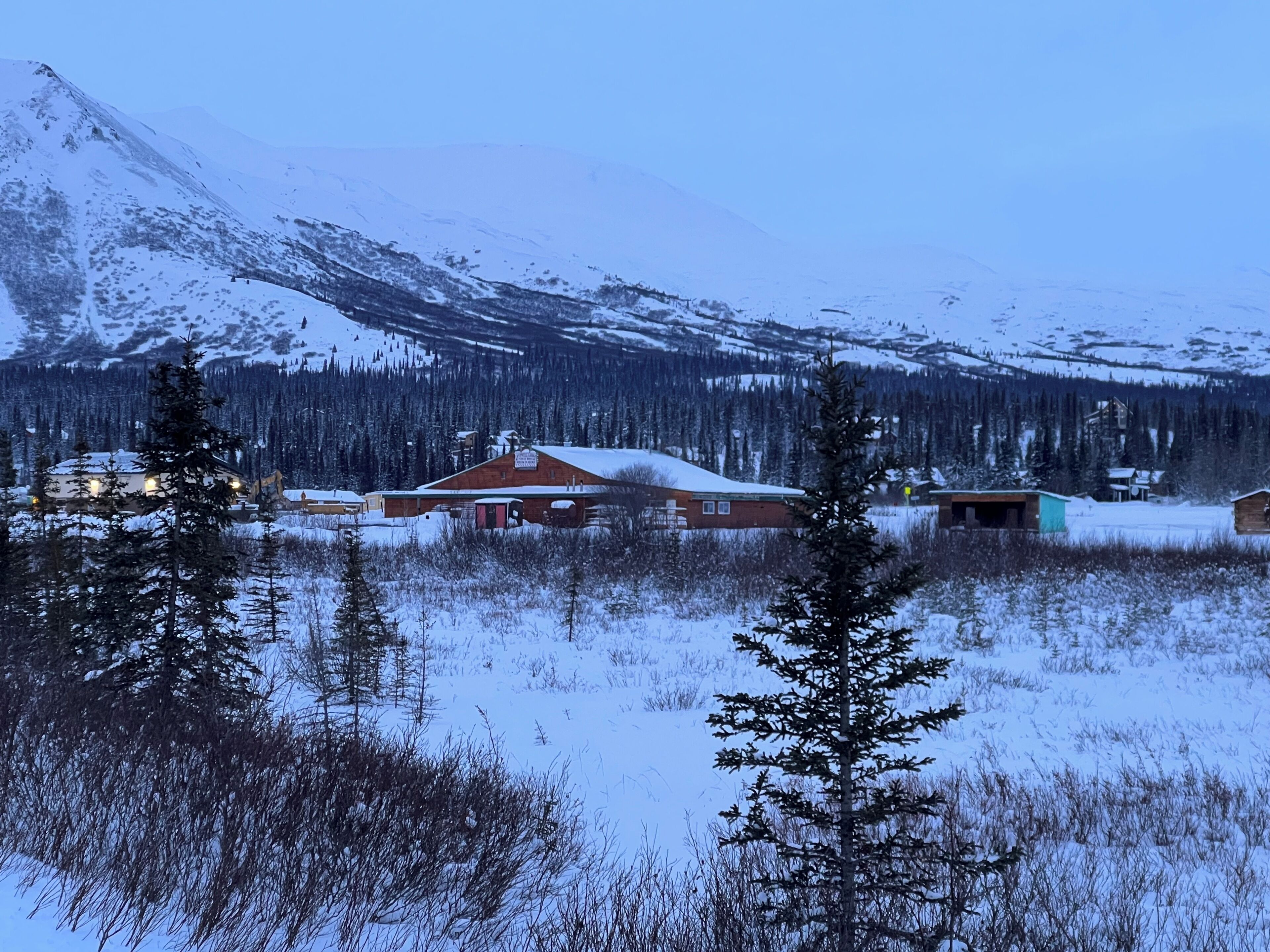 A snow-covered landscape with a cabin and a mountain in the background.