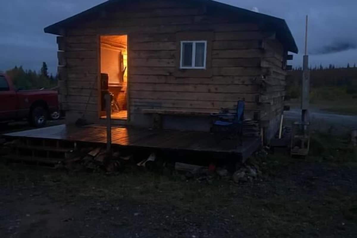 A log cabin with an open door, a small window, and a wooden deck.