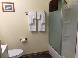 Un baño con inodoro, ducha con puerta de vidrio y dos toallas blancas colgadas en un perchero metálico.
