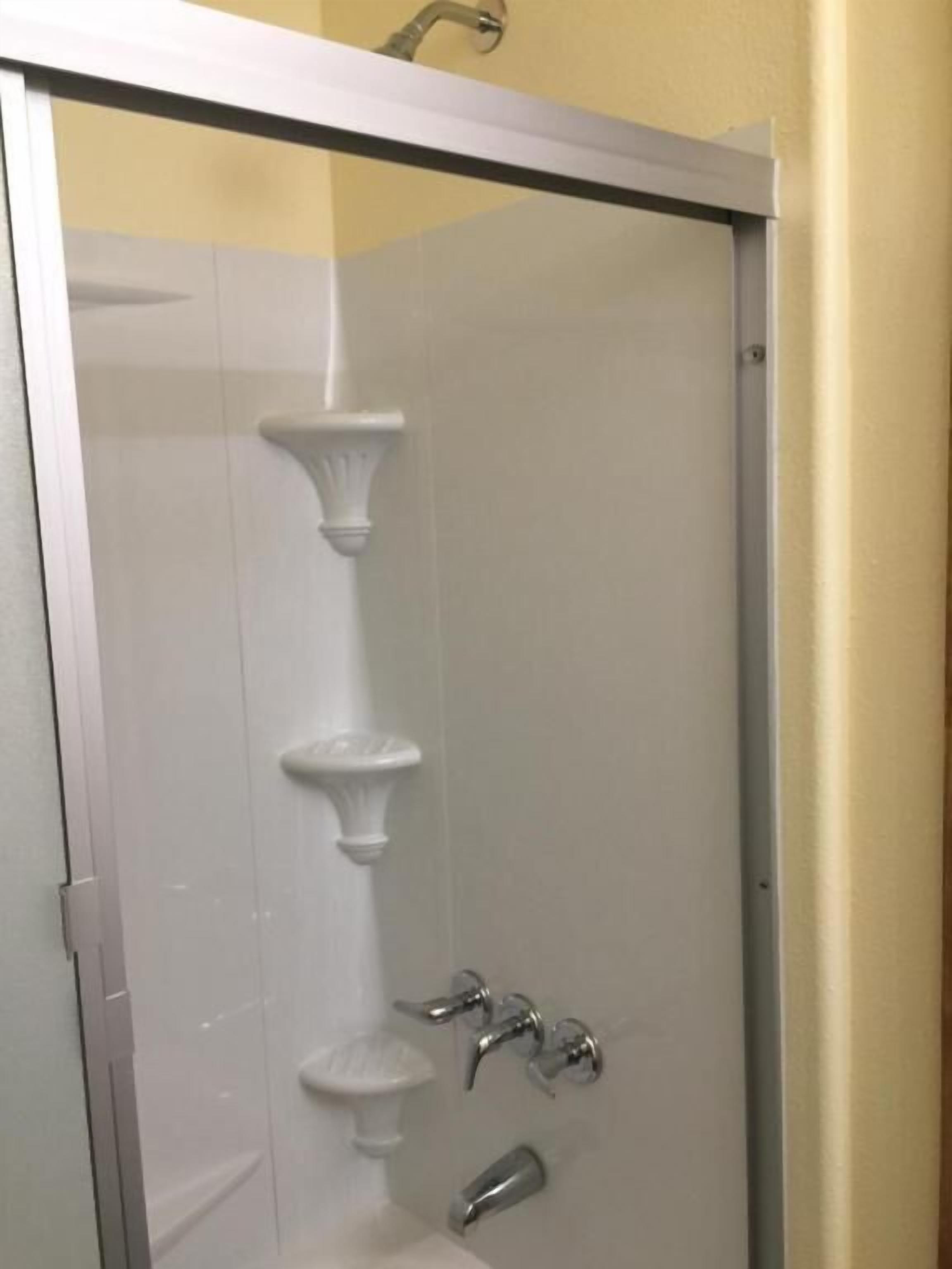 Um chuveiro com porta de vidro, torneira fixada na parede e chuveiro manual.