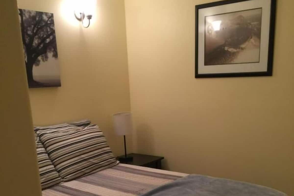 A bed with striped bedding, a wall-mounted lamp, and a framed picture on the wall.