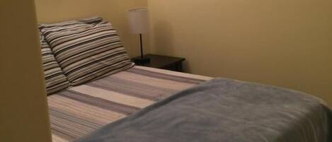 A bed with striped bedding, a wall-mounted lamp, and a framed picture on the wall.