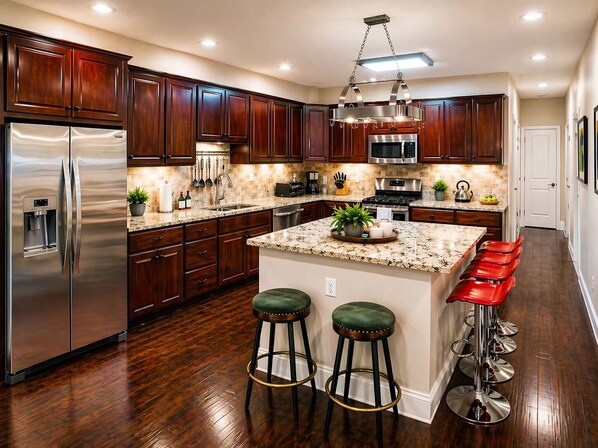 Una cocina moderna con armarios de madera oscura, electrodomésticos de acero inoxidable, encimeras de granito y una isla central con taburetes de bar.