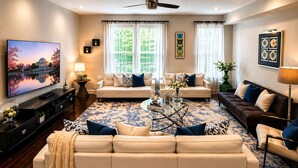 A modern living room with a large flat-screen TV, two sofas, a coffee table, and a ceiling fan.