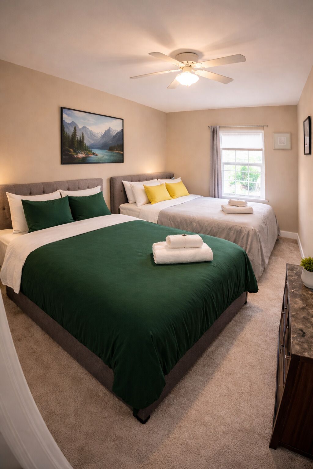 Une chambre d’hôtel avec deux lits, un ventilateur de plafond, une fenêtre avec des rideaux et un tableau au mur.