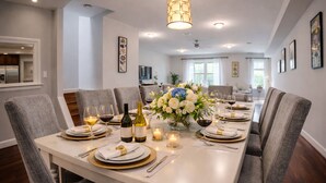 A dining room with a long table set for a meal, chairs, a chandelier, and a vase of flowers.