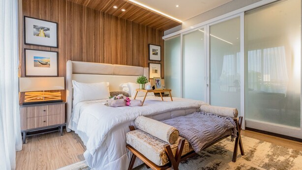 Un dormitorio moderno con una cama grande, una mesita de noche, un banco y un ventanal corredizo.