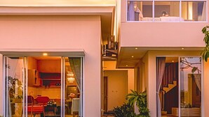 Una casa moderna de dos pisos con balcón, ventanas amplias y una cocina a la vista.