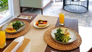 Un comedor con una mesa dispuesta para el desayuno, incluyendo platos de comida, un vaso de zumo de naranja y un posavasos tejido.