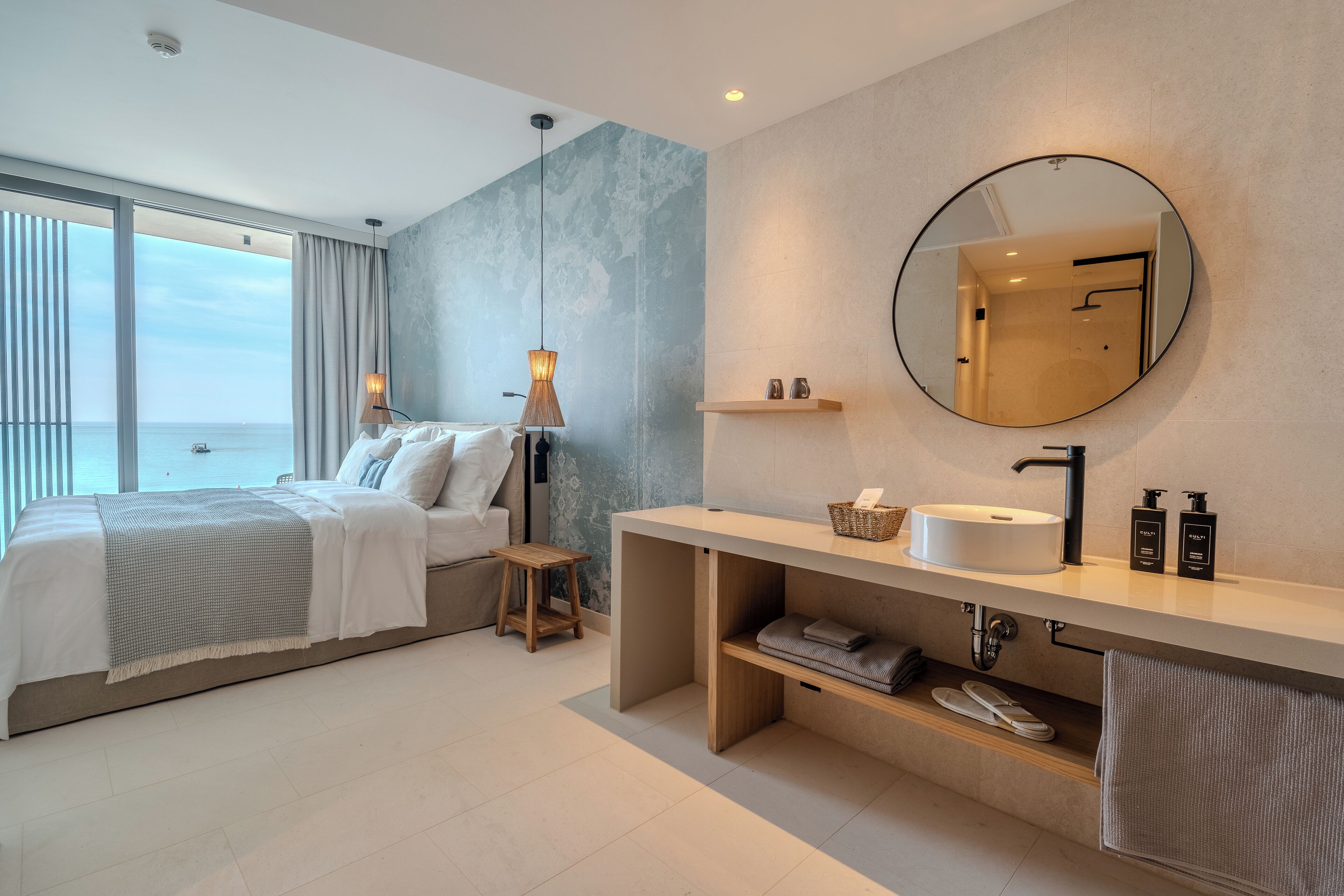 Een moderne hotelkamer met een groot bed, een ronde spiegel, een wastafel en uitzicht op zee.