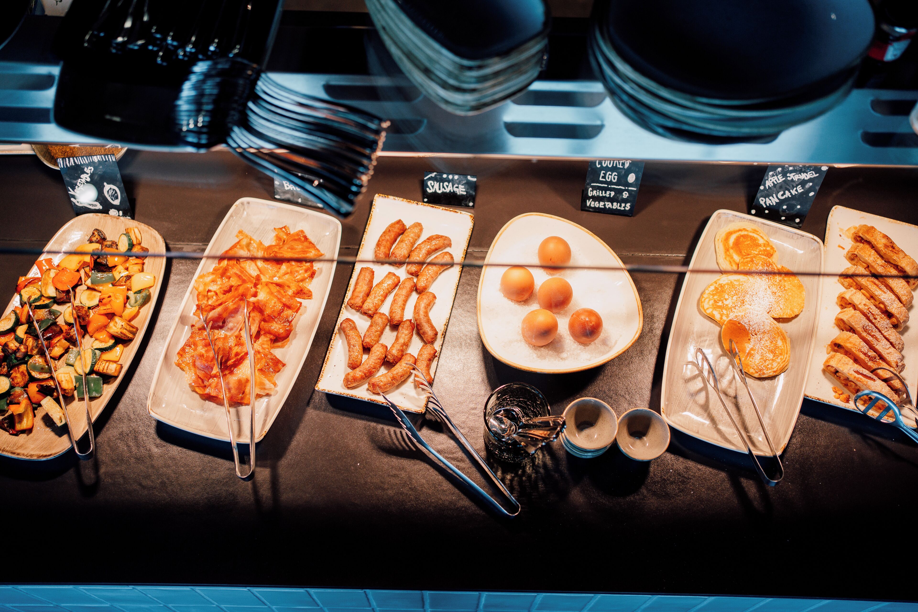 Un buffet proposant une variété de plats, notamment des légumes, des saucisses et des desserts.