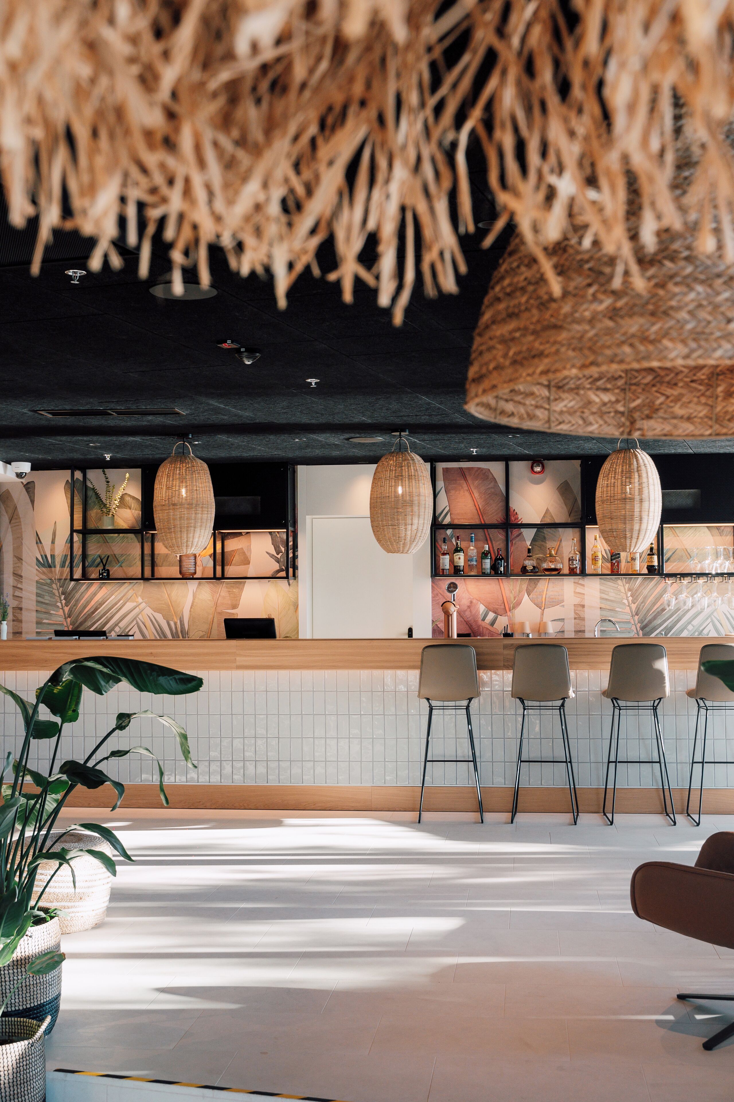 A modern bar area with a thatched ceiling, wicker pendant lights, and a white tiled bar counter.