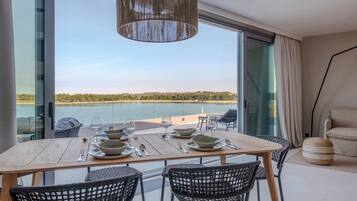 Comedor con mesa dispuesta para cuatro, vistas a un cuerpo de agua, amplia ventana y lámpara colgante moderna.