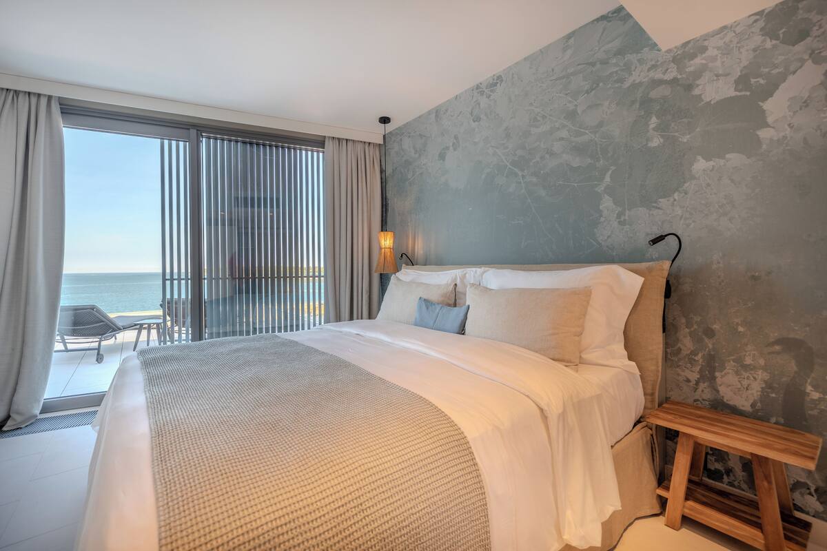 Ein Hotelzimmer mit einem großen Bett, Meerblick und einem Balkon mit einem Stuhl.