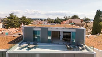 Een modern huis met een glazen balkon, buitenmeubels en uitzicht op de omgeving.