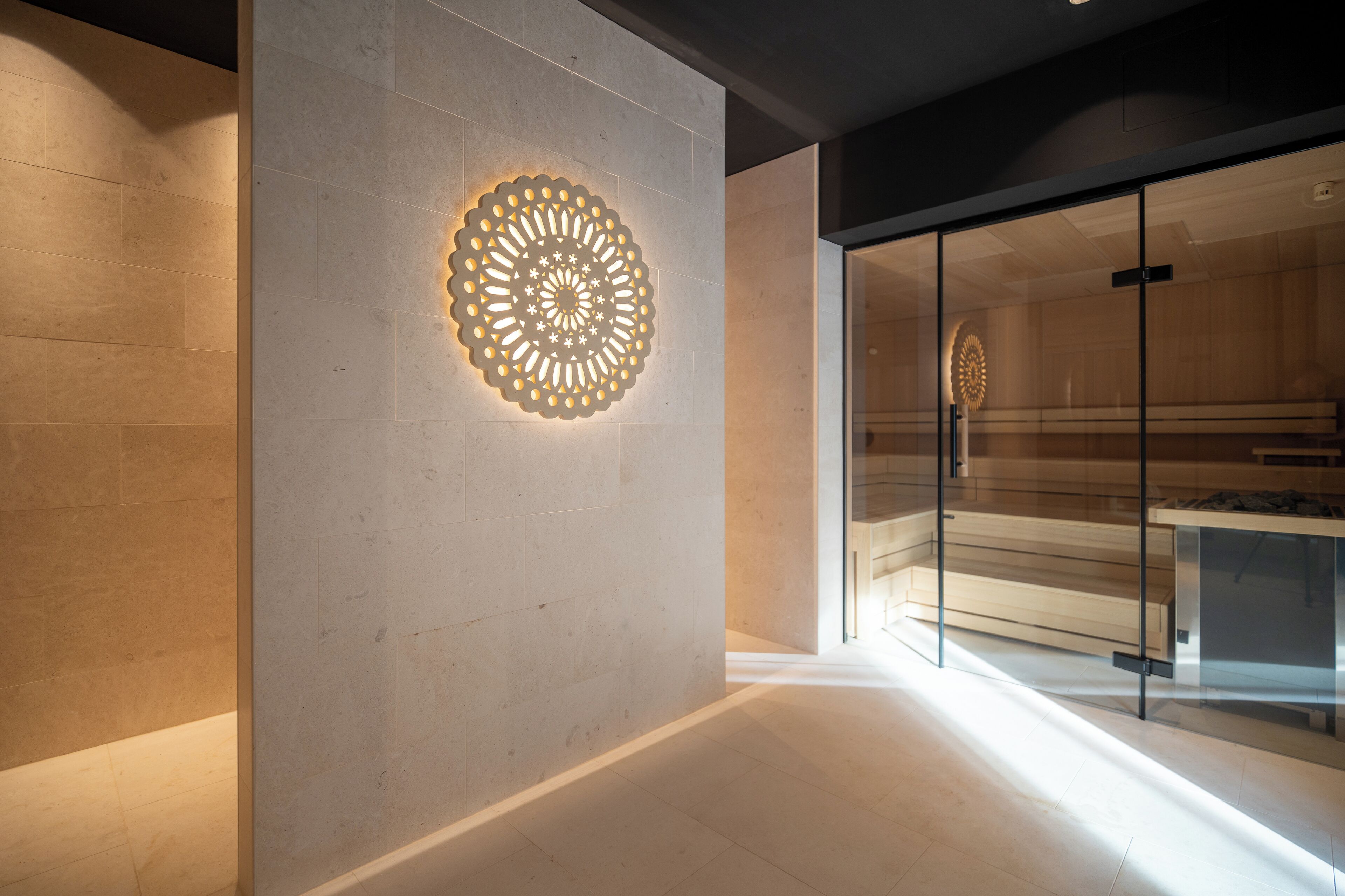 A modern interior with a circular light fixture on a wall, a glass partition, and a wooden bench.
