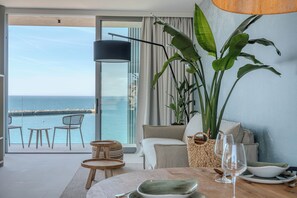 Ein modernes Zimmer mit Balkon und Meerblick, ausgestattet mit einer Sitzecke, einem Esstisch mit Stühlen und einer großen Pflanze.