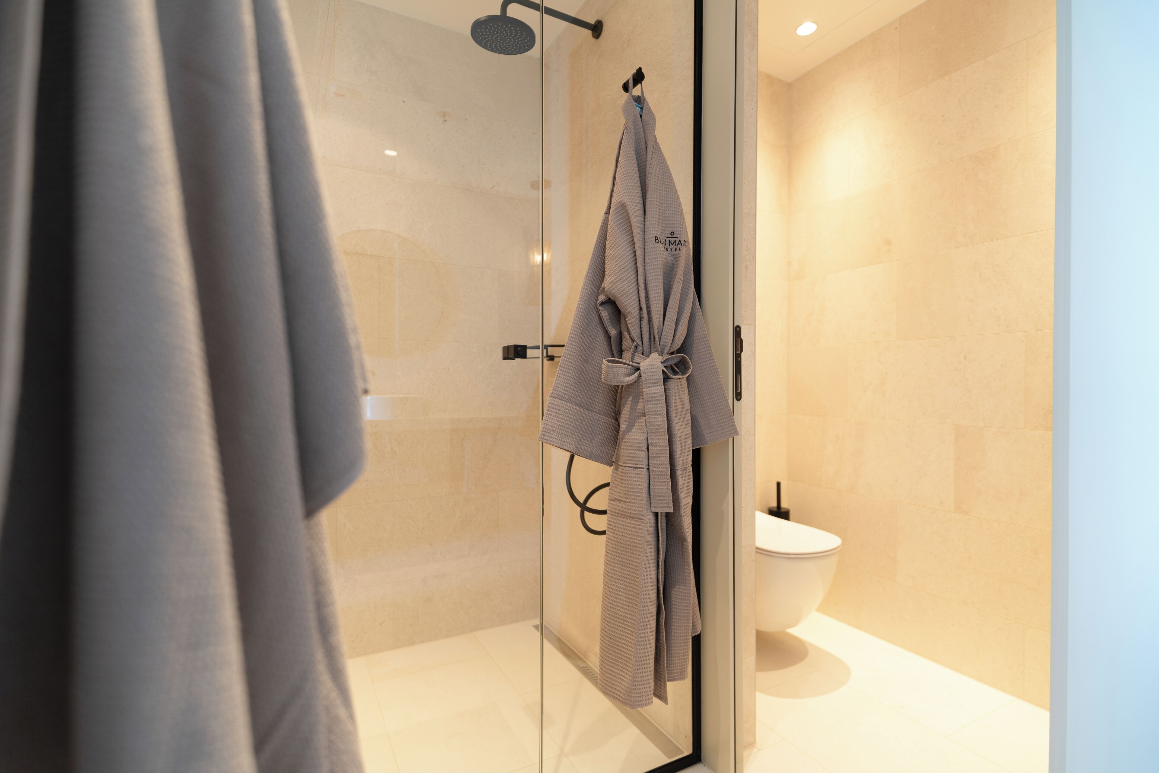 Un baño moderno con cabina de ducha de vidrio, inodoro blanco y un perchero con toalla.