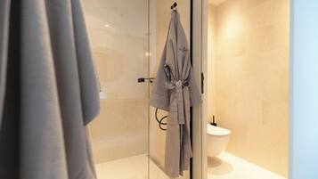 Un baño moderno con cabina de ducha de vidrio, inodoro blanco y un perchero con toalla.