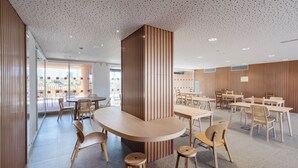 A modern interior with round tables and wooden chairs, a perforated ceiling, and wooden panel walls. -  Valencia Tower (Burjasot)