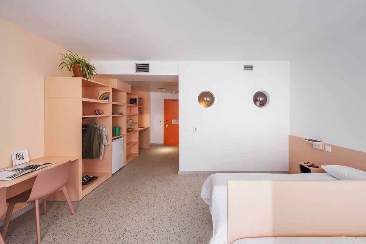 Une chambre d’hôtel moderne équipée d’un lit, d’un bureau, d’une armoire et d’une salle de bain visible à travers une porte ouverte.