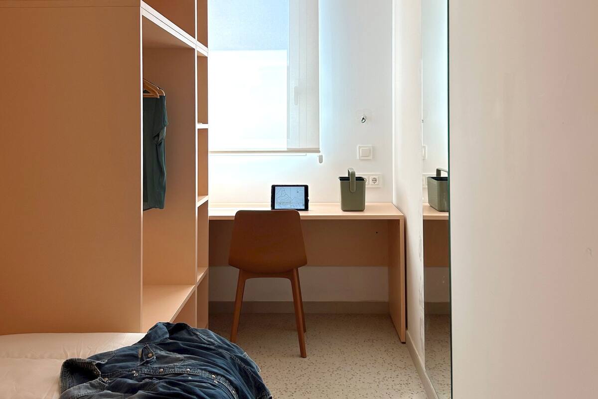 Une chambre à coucher comprenant un lit, un bureau, une chaise, une armoire et un grand miroir.