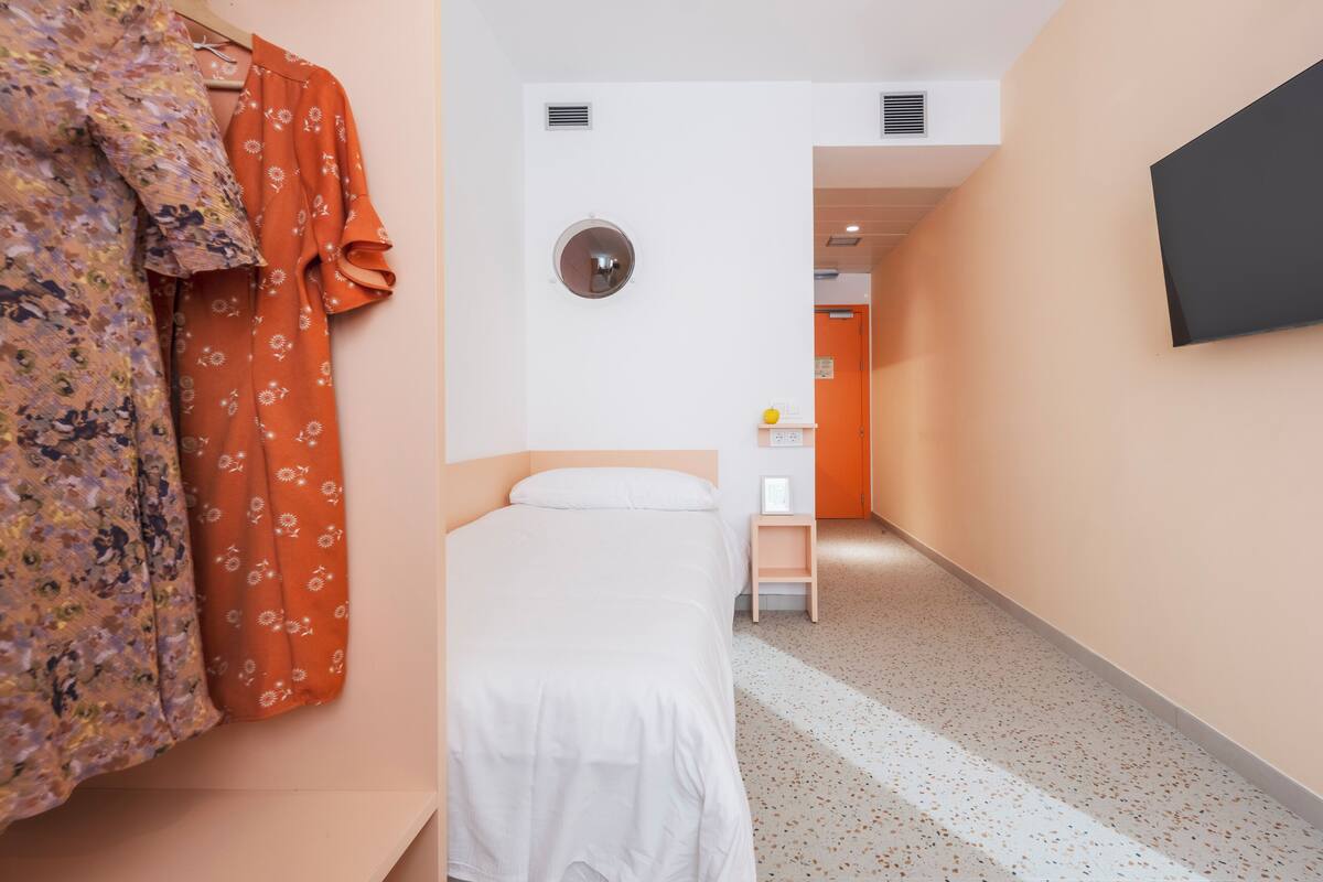 Une chambre d’hôtel équipée d’un lit, d’un petit bureau, d’une chaise et d’un téléviseur fixé au mur.