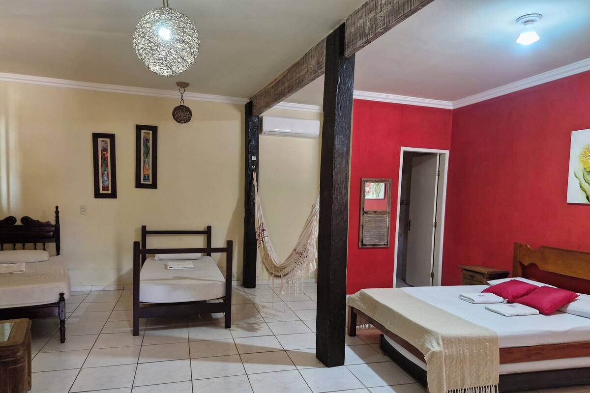 Une chambre d’hôtel avec un lit, une chaise, un hamac, un luminaire au plafond et une porte.