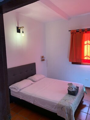 A single bed with a grey headboard, a small bedside table with a basket, and a wall-mounted light fixture. - Fatima Hostel Santa Marta (Santa Marta)