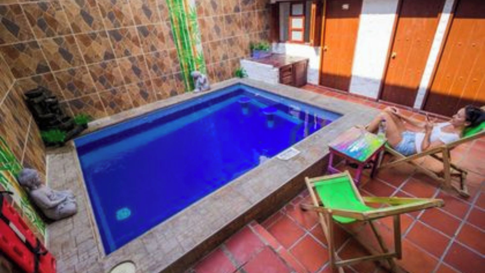 A small swimming pool with a tiled deck, a wooden chair, and a table.