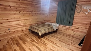Una habitación con paneles de madera, una cama, un ventilador de techo y una ventana con cortinas.