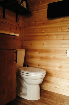 A wooden cabin interior with a white toilet, wooden cabinets, and a shelf with a bottle.
