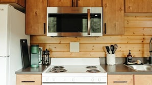 Una cucina con mobili in legno, un forno a microonde in acciaio inox, un fornello bianco e diversi utensili da cucina.