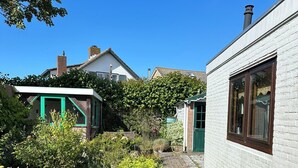 A narrow brick pathway flanked by lush greenery and white brick buildings with green doors and windows.