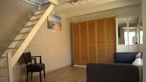 A room with a wooden staircase, a wooden wardrobe, a grey sofa, and a wooden floor.